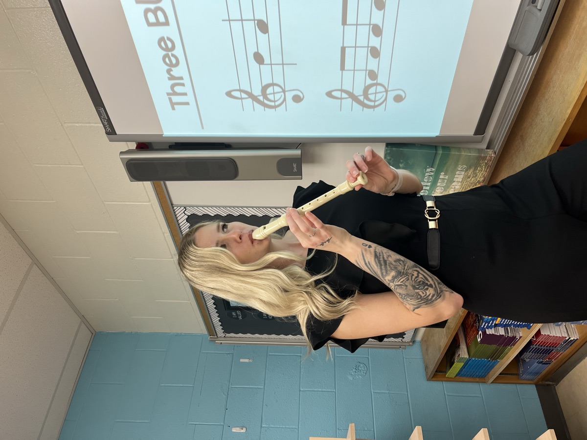 Danielle teaching a music lesson at the SMART board, recorder in hand